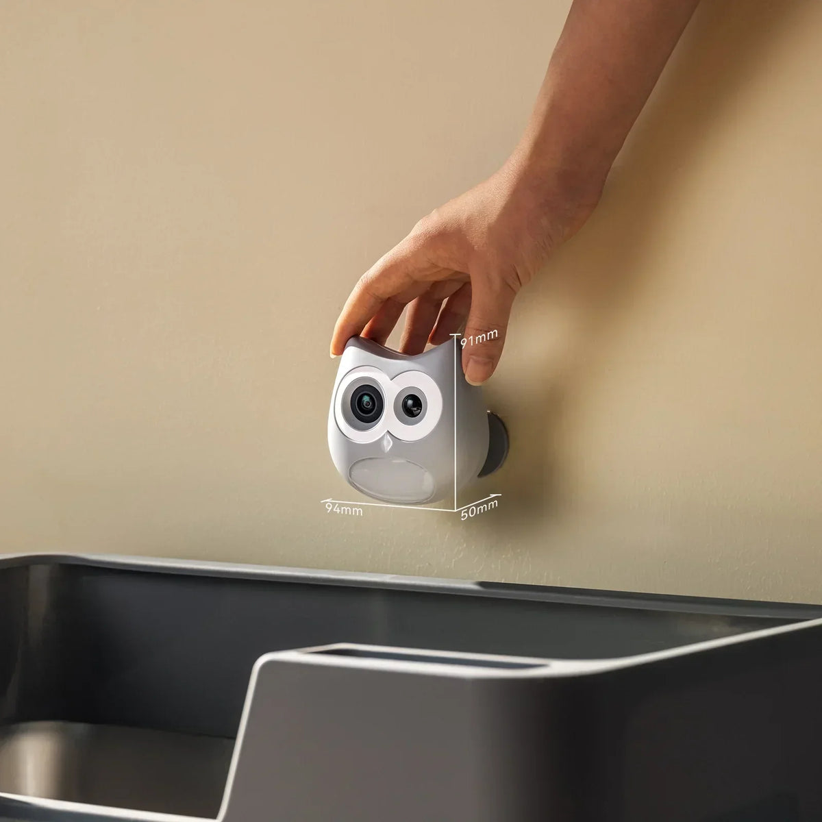 Hand installing SiiPet LitterLens owl‑shaped cat litter box camera on wall, dimension markings showing compact device size next to litter box